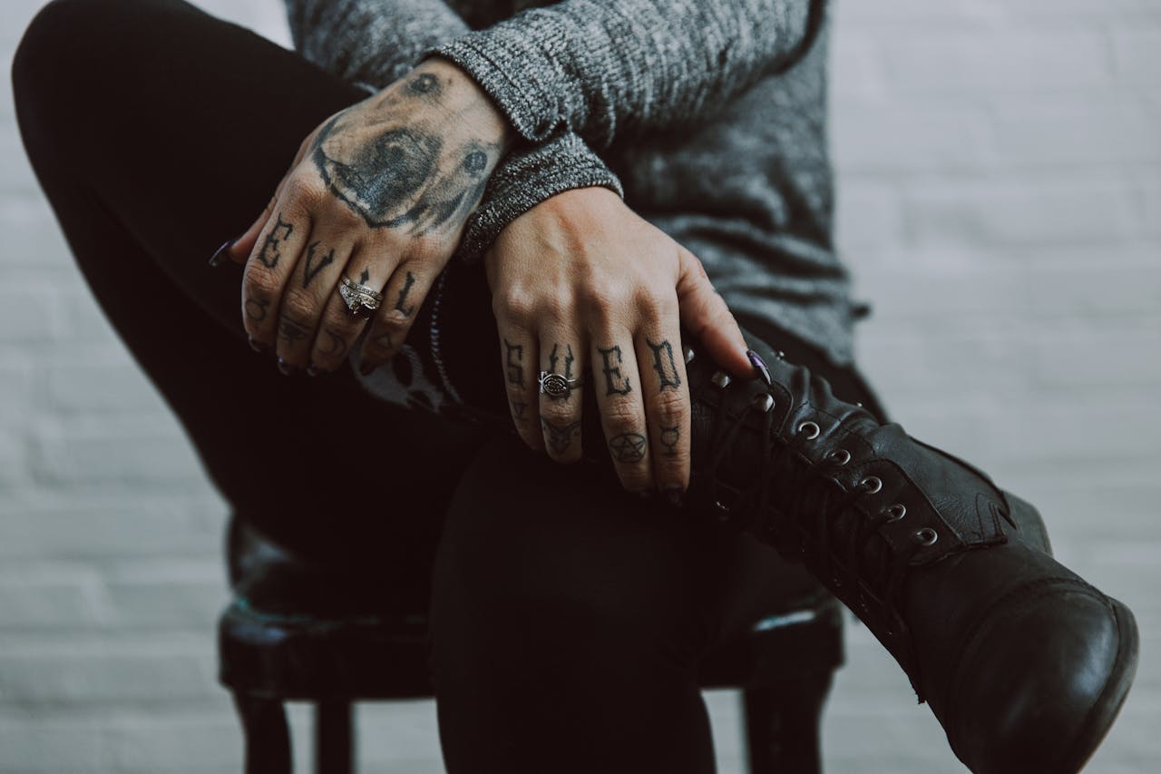 Close-up of tattooed hands and rings resting on black boots, creating a moody and artistic vibe.