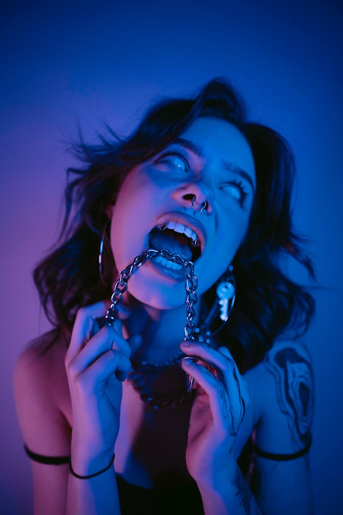 Alternative girl with tattoos holding a chain in a dramatic blue light studio shoot.