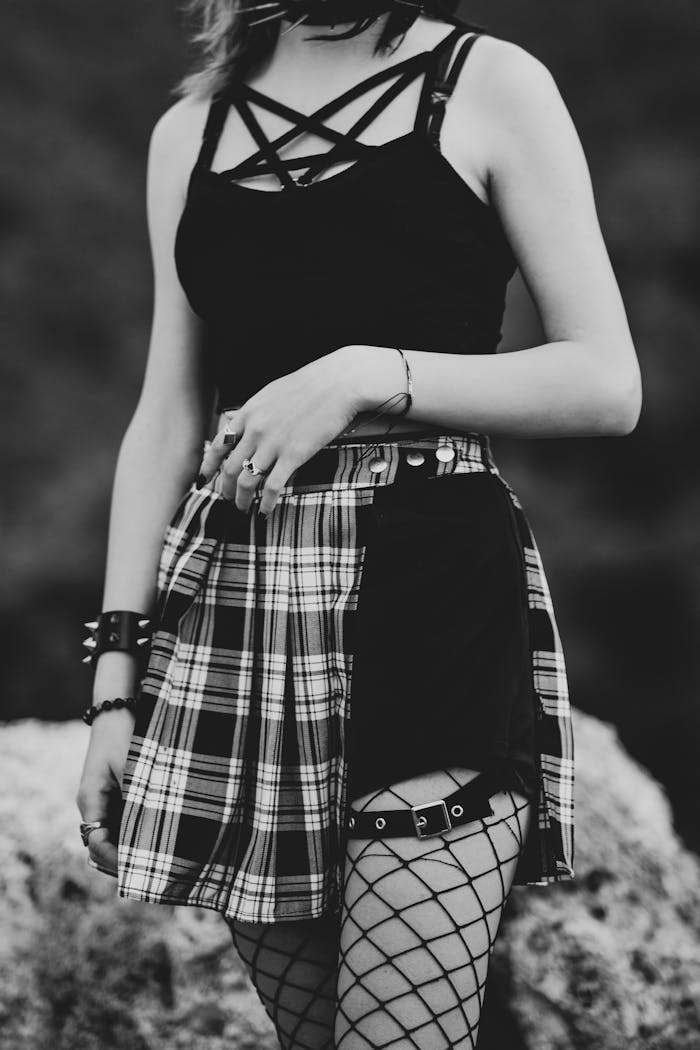 Black and white shot of a woman in goth fashion with plaid skirt and fishnets.
