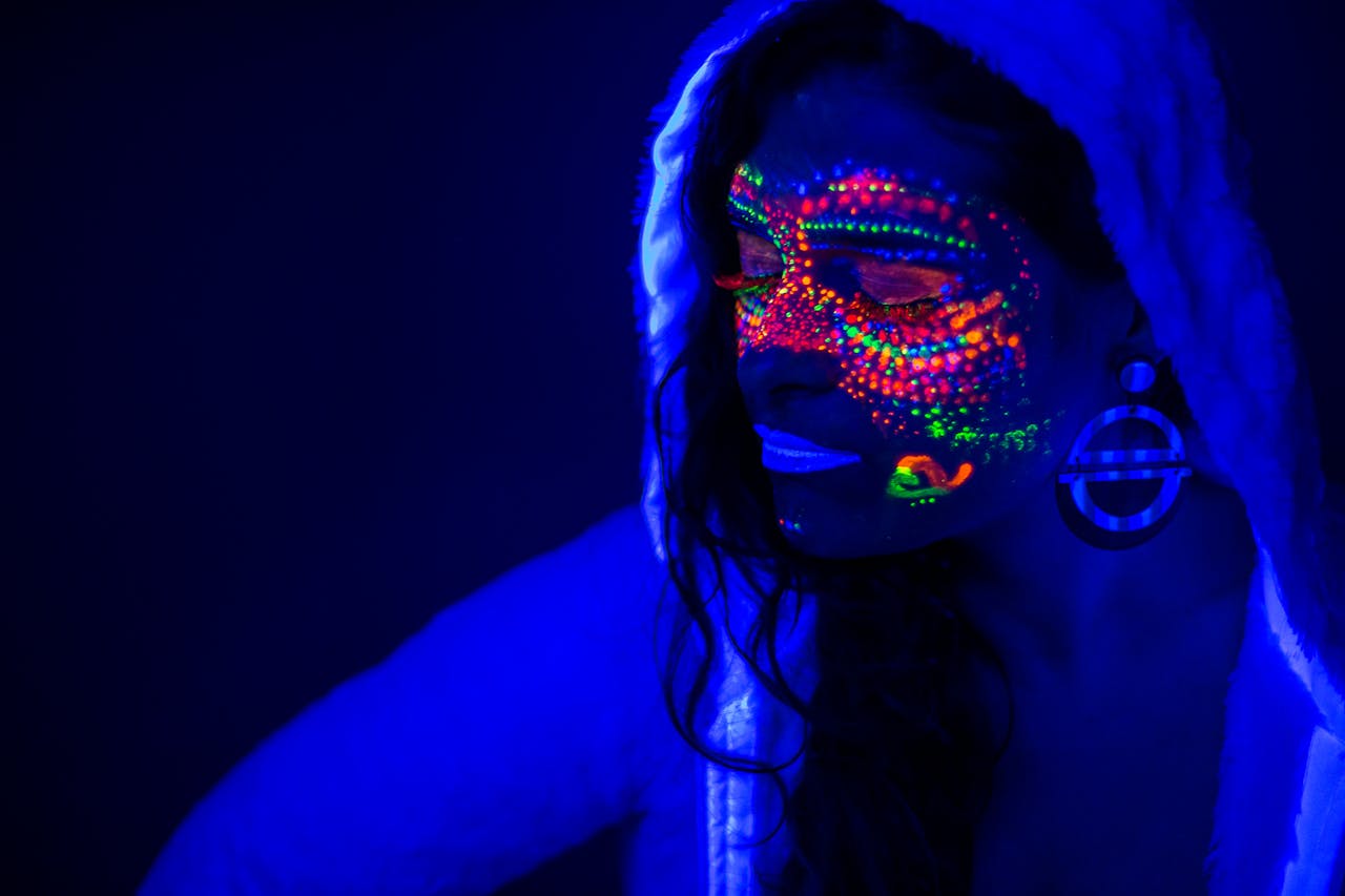 Portrait of a woman with glowing neon paint under UV light creating a futuristic effect.