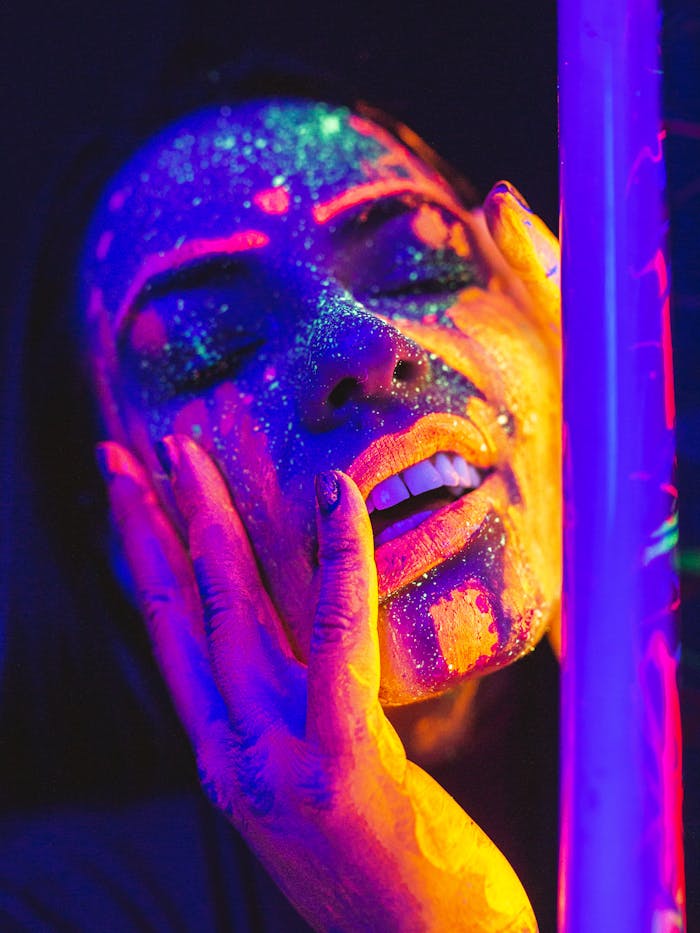 Close-up portrait of a woman with luminous neon face paint under a blacklight, showcasing vibrant colors.