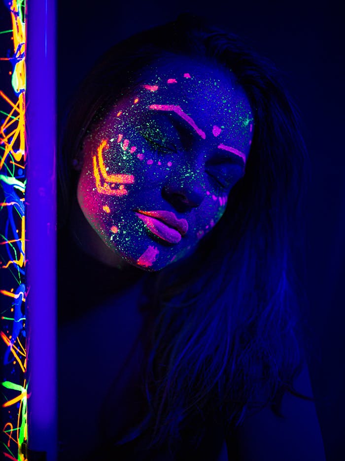 Portrait of a woman with glowing neon paint under UV light, eyes closed in tranquil expression.