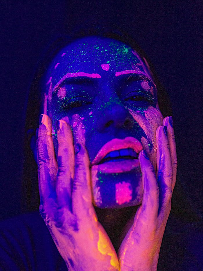 Striking portrait of a woman with glowing UV makeup under neon lights, showcasing artistic creativity.